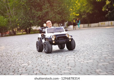 Cute 2 Year Old Boy In A White T Shirt Is Riding A White Electric Car In The Park