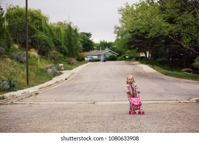 Cute 2 Year Old Walking On The Road With A Toy Stroller