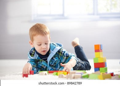 Cute 3 Year Old Boy Laying On Floor, Playing With Cubes.?