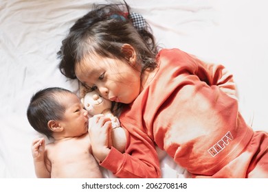 A cute 3 years old asian big sister is smiling and playing with her newborn baby brother with fully happiness moment in the morning time.