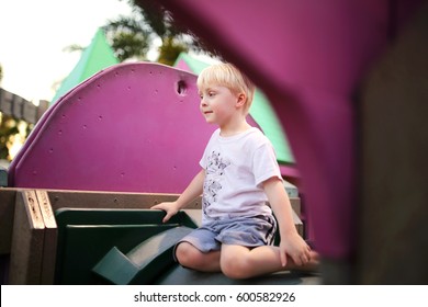 A Cute, 4 Year Old, Preschool Child Is Sitting Alone On The Jungle Gym At The School Playground, Playing By Himself.