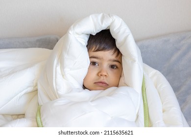 Cute 4 Years Old Boy Turned Wrapped Into White Soft Blanket Is Making Different Faces. Kid Is Happy, Amazed, Has Serious Face Or Is Smiling. Happy Boy Is Having Fun Before Bedtime. Child's Emotions.