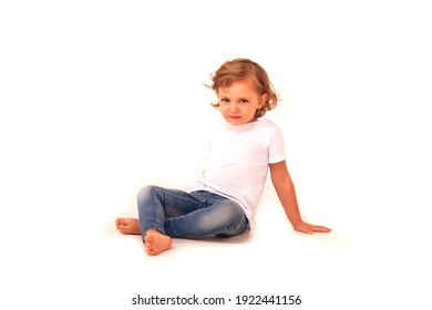 Cute 4-5 Year Old Girl In Jeans And T-shirt On White Isolated Background Looks At Camera. Concept Playing And Children Recreation. Little Child In Casual Clothes Posing And Showing Emotions