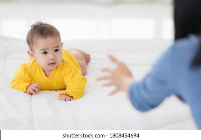 Cute 6 months Asian baby try to crawl and move on floor looking to mom while her mether beckoning hand and cheer up for her. Idea for happiness relationship between parenthood and toddler in family.