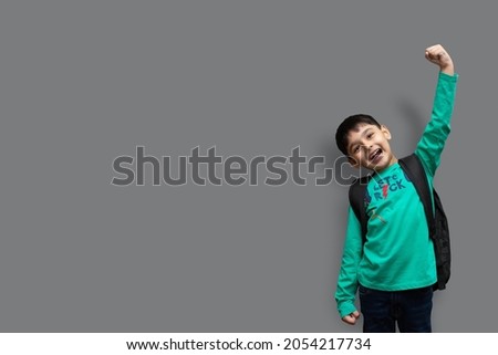 Cute 7 year-old happy boy with school backpack holding books in plain background for education concept