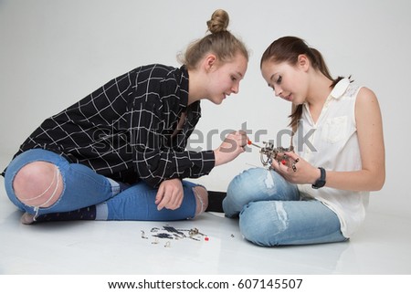 Cute and absorbed teenage girls sitting on the floor mounting a little metal helicopter model
