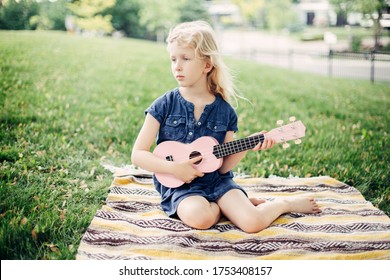 Cute Adorable Blonde Girl Playing Pink Guitar Toy Outdoor. Child Playing Music And Singing Song In Park. Hobby Activity For Children Kids. Tender Memorable Authentic Candid Childhood Moment. 