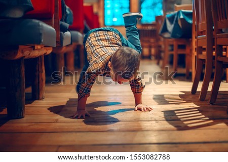 Cute adorable boy three years old having fun in cafe restaurant. Child playing on floor in public place. Freedom of self expression and behaviour for kids. Toddler touching dirty ground.