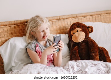 Cute Adorable Caucasian Girl Stay At Home And Call Her Friends On Smartphone. Child Kid Having Face Time Call Talk With People Relatives While On Self Isolation During Quarantine Of COVID-19.