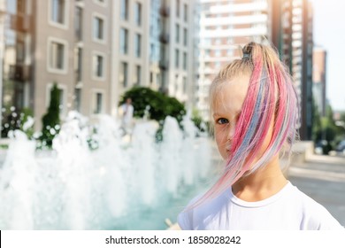 Cute adorable caucasian little kid girl and multicolored pastel chalk painted dyed blond hair city street and fountain background  Female child portrait pink colorful hairstyle smiling outdoors