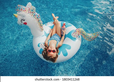 Cute Adorable Girl In Sunglasses With Drink Lying On Inflatable Ring Unicorn. Kid Child Enjoying Having Fun In Swimming Pool. Summer Outdoor Water Activity For Kids. View From Above Overhead.