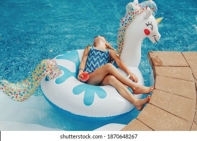 Cute Adorable Girl In Sunglasses With Drink Lying On Inflatable Ring Unicorn. Kid Child Enjoying Having Fun Relaxing Resting In Swimming Pool On Floatie. Summer Outdoor Water Activity For Kids. 