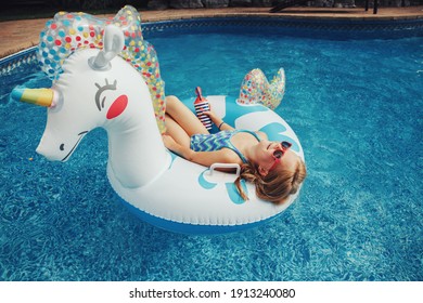 Cute Adorable Girl In Sunglasses With Drink Lying On Inflatable Ring Unicorn. Kid Child Enjoying Having Fun Relaxing Resting In Swimming Pool On Floatie. Summer Outdoor Water Activity For Kids. 