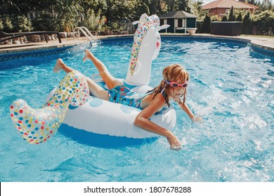 Cute Adorable Girl In Water Goggles Lying Chilling On Inflatable Ring Unicorn. Kid Child Enjoying Having Fun In Swimming Pool. Summer Outdoor Water Activity For Kids. 