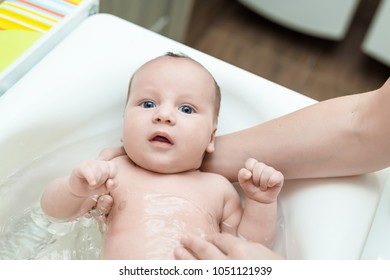 Cute adorable infant boy having first bath. Mother washes baby with comfortable temperature water. Newborn hygiene and healthcare concept - Shutterstock ID 1051121939