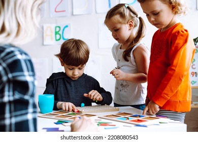 Cute, Adorable Little Boy Do Logic Motor Exercise With Figures In Class Group. Teacher With Children Having Fun And Learning In Kid Development Childcare Center For Preschoolers. Early Education Group