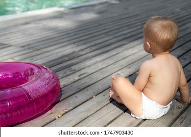 Cute Adorable Little Caucasian Blond Toddler Boy Kid In Diaper, Inflatable Ring Sitting Near Poolside On Wood Flooring At Pool Edge Before Swimming. Happy Child Enjoy Summer Vacation Travel Family