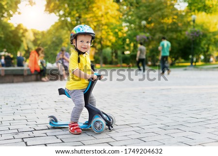 Cute adorable little caucasian toddler boy portrait in helmet having fun riding three-wheeled balance run bike scooter in city park or forest. Child first bike. Kids outdoor sport activities.