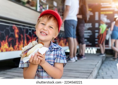 Cute adorable little happy smiling boy kid enjoy eating hot dog sausage in bread near street cafe stall outdoors. Child healthy eating lunch hotdog. Junk food and fast food unhealthy snack concept - Powered by Shutterstock