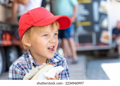 Cute adorable little happy smiling boy kid enjoy eating hot dog sausage in bread near street cafe stall outdoors. Child healthy eating lunch hotdog. Junk food and fast food unhealthy snack concept - Powered by Shutterstock