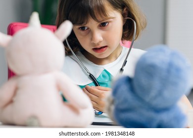 Kleine, süße, jugendliche Mädchen tragen eine medizinische Uniform, die das Stethoskop hält und kranken Spielzeugpatienten zuhört. Kluges Kleinkind, das Krankenhausspiel als Arzt vorgibt Krankenschwester Konzept.