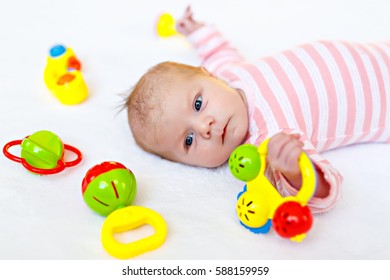 Cute Adorable Newborn Baby Playing With Lots Of Colorful Rattle Toys On White Background. New Born Child, Little Girl Looking Surprised At The Camera. Family, New Life, Childhood, Beginning Concept