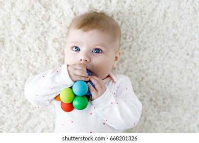 Cute adorable newborn baby playing with colorful wooden rattle toy ball on white background. Sweet happy girl with blue eyes