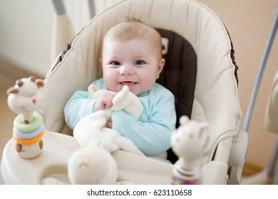 Cute adorable newborn baby sitting in swing. Closeup of peaceful child, little baby girl swinging and playing. Looking on toys. Family, birth, new life. Attentive child. Tiny girl and soft plush toy