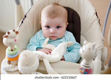 Cute adorable newborn baby sitting in swing. Closeup of peaceful child, little baby girl swinging and playing. Looking on toys. Family, birth, new life. Attentive child. Tiny girl and soft plush toy