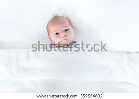 Cute adorable newborn baby in white bed and wrapped in blanket. New born child, little girl looking surprised at the camera. Family, new life, childhood, beginning concept.