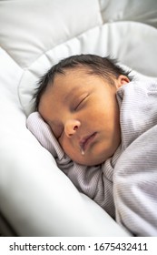 A Cute Adorable Newborn Mixed Race Infant Baby Girl With Dark Brown Hair Sleeping On Her Side In Her Bassinet Peacefully With Her Eyes Closed And Milk Drool Running Out Of Her Closed Lips.