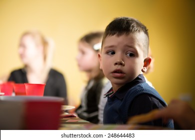 Cute Adorable Preschooler Boy Sitting In Kindergarten Looking Confused.Sad Child In Kindergarten.Bored Kid In Preschool/kindergarten/nursery.Bored Nervous Boy At Children Birthday Party