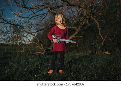 Cute Adorable Young Girl Playing Guitar Toy Outdoor. Girl Pretending To Be A Rock Music Star. Adorable Funny Child Having Fun In Park. Weird Funny Hilarious Authentic Candid Childhood Moments. 