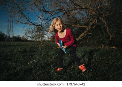 Cute Adorable Young Girl Playing Guitar Toy Outdoor. Girl Pretending To Be A Rock Music Star. Adorable Funny Child Having Fun In Park. Weird Funny Hilarious Authentic Candid Childhood Moments. 