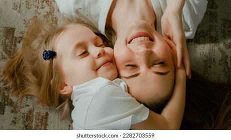 Cute affectionate adopted little kid preschool girl hugging cuddling mother head top view. Child daughter with mum two faces cuddle lying down at home talking smiling with eyes closed tender moment - Powered by Shutterstock