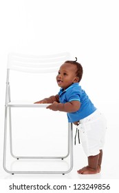 Cute African American Baby Boy Learning To Walk Around A Chair