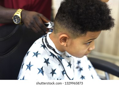 Cute african american boy in the african barbershop. Cute mixed boy makes a haircut in the African salon. Hair style. Haircut by machine for children. School boy hair style. Haircut by scissors.  - Powered by Shutterstock