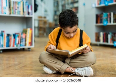 cute african american boy sitting on floor and reading book 