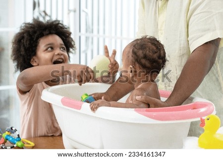 Cute African American brother helping dad to wash baby sister in bathtub, cleaning the body for good health, man taking care of child