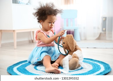 Cute African American child imagining herself as doctor while playing with stethoscope and toy bunny at home - Powered by Shutterstock