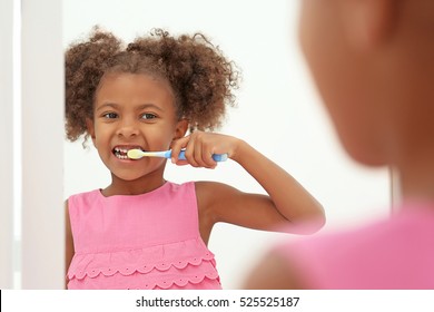 Cute African American Girl Brushing Teeth And Looking In Mirror In Bathroom