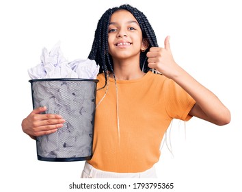 Cute African American Girl Holding Paper Bin Full Of Crumpled Papers Smiling Happy And Positive, Thumb Up Doing Excellent And Approval Sign 