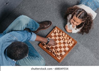 Cute African American Girl Playing Chess With Father On Floor At Home