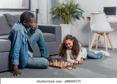 Cute African American Girl Playing Chess With Father On Floor At Home