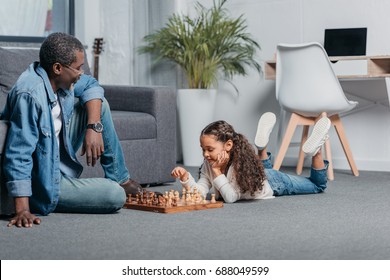 Cute African American Girl Playing Chess With Father On Floor At Home