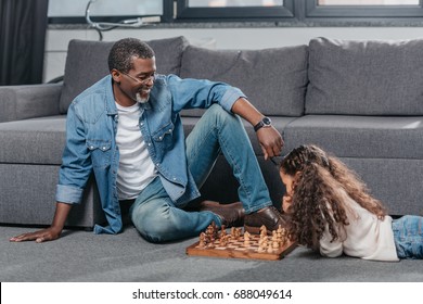 Cute African American Girl Playing Chess With Father On Floor At Home