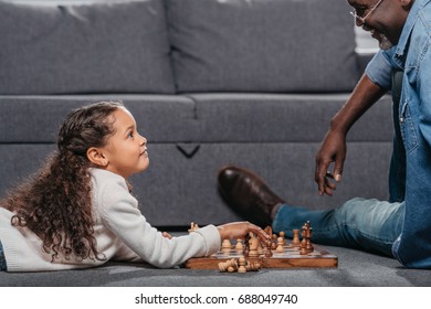 Cute African American Girl Playing Chess With Father On Floor At Home