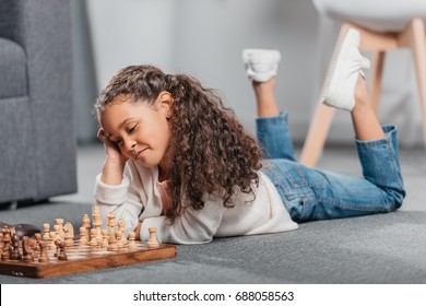 Cute African American Girl Playing Chess On Floor At Home