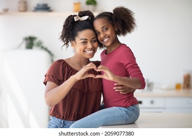 Cute African American Mother And Daughter Embracing And Showing Heart Shaped Gesture With Their Palms, Happy Black Family Single Mom And Teen Girl Kid Cuddling At Kitchen, Copy Space