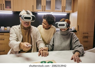 Cute African boy looking at his grandfather in vr headset pressing button of remote control while standing between grandparents